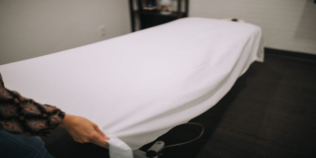image of a female placing a white poly/cotton flat sheet over a massage table